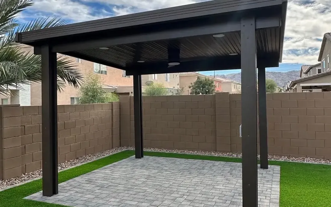 Solid-roof black pergola with a ceiling fan shading pavers beside artificial turf